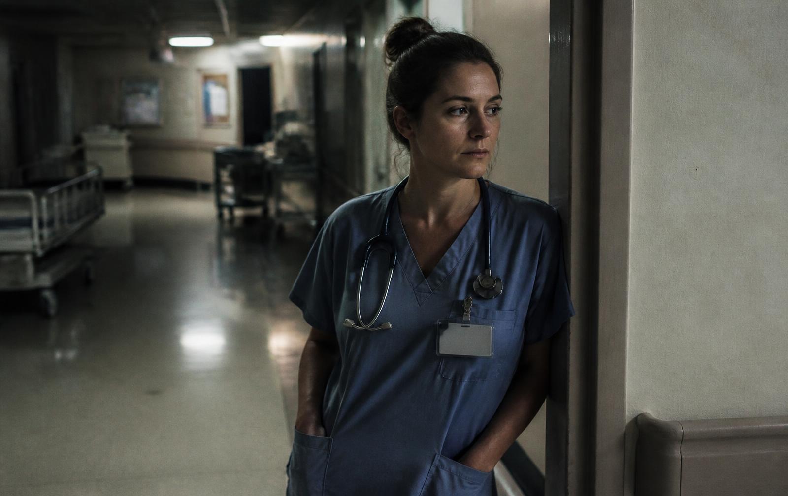 A night-shift nurse in scrubs pausing in a hospital corridor before dawn